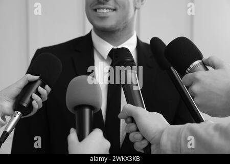 Uomo d'affari che fa un colloquio ai giornalisti al chiuso, primo piano. Effetto bianco e nero Foto Stock