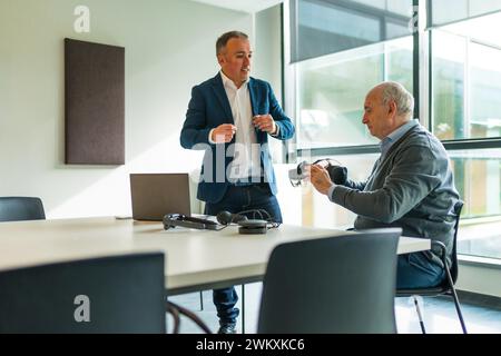 Uomo d'affari che presenta un nuovo e innovativo visore per la realtà virtuale a un cliente in ufficio Foto Stock