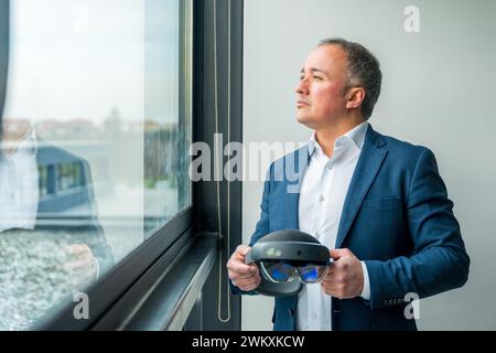 Uomo d'affari che guarda attraverso la finestra con futuristici occhiali di protezione per la realtà virtuale che si concentrano sul futuro di successo Foto Stock