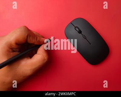 Qualcuno che tiene la matita con un mouse wireless nero su sfondo rosso. Foto Stock