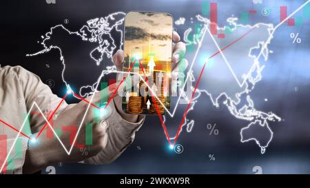 Primo piano mano maschile che mostra e punta il telefono cellulare con un grafico delle scorte in crescita sullo sfondo della mappa mondiale. Commercio, azioni e conc. Economico globale finanziario Foto Stock