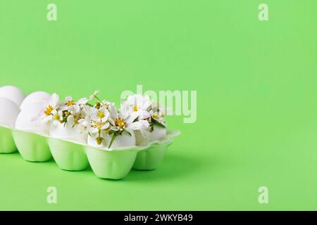 Uova bianche nel vassoio delle uova con pera primaverile e fiori di fragola su sfondo verde. Buona Pasqua Foto Stock