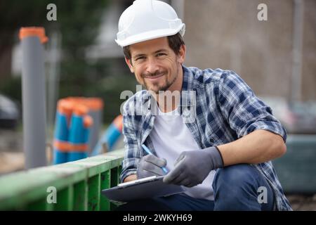 ingegnere civile accovacciato che indossa un elmetto che lavora in cantiere Foto Stock