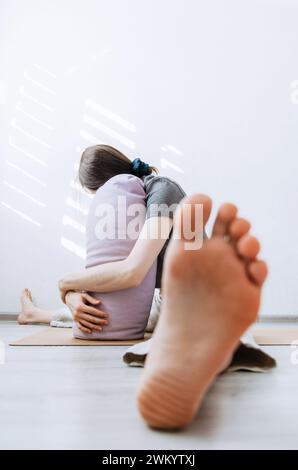 Donna in abbigliamento casual che pratica yin yoga gamba larga piegata in avanti posa appoggiata sul sostegno Foto Stock