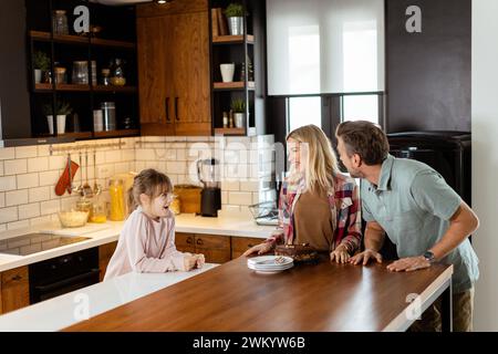 Una scena emozionante si svolge mentre una famiglia assaggia insieme una deliziosa torta al cioccolato nel calore della sua cucina soleggiata, condividendo sorrisi e sorrisi Foto Stock