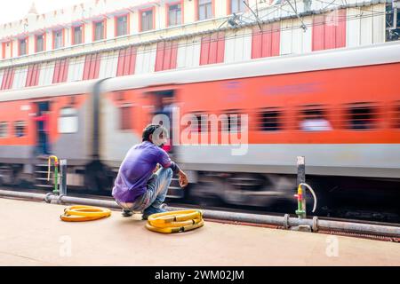 Un dipendente della Indian Railways che aspetta su un binario mentre passa un treno Foto Stock