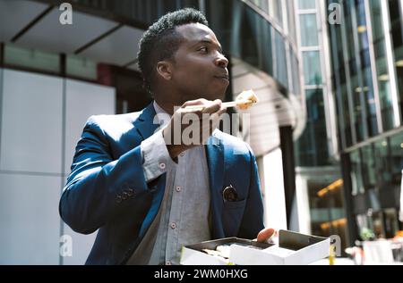 Uomo d'affari che mangia sushi con bacchette davanti agli edifici Foto Stock