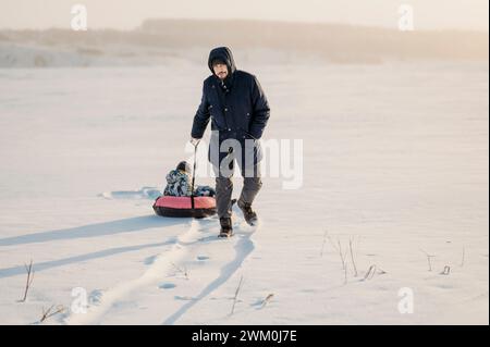 Uomo che tira un bambino seduto su un tubo gonfiabile nella neve Foto Stock