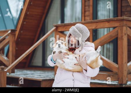 Giovane donna sorridente che tiene il cane Corgi davanti alla capanna di legno Foto Stock