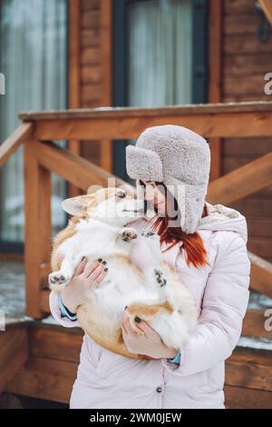 Giovane donna che tiene il cane Corgi davanti alla cabina di legno Foto Stock