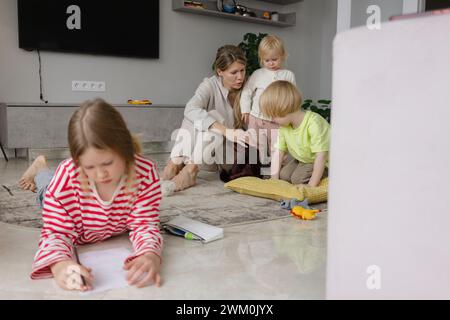 I bambini giocano con la madre e la ragazza che fanno i compiti a casa Foto Stock