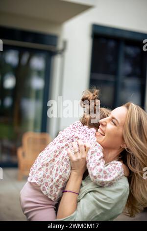 Donna allegra che abbraccia figlia vicino a casa Foto Stock