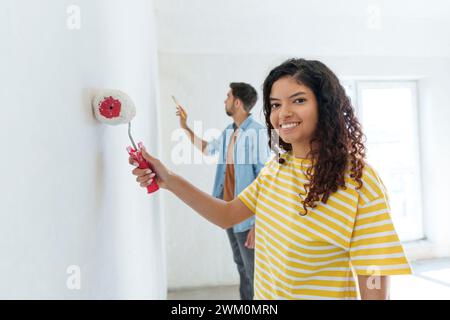 Donna sorridente con rullo di pittura in piedi vicino a un uomo nella nuova casa Foto Stock