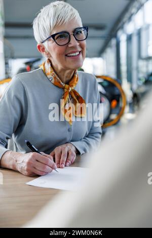 Una donna anziana felice che fa i documenti alla scrivania Foto Stock