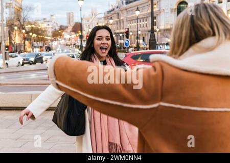 Donna eccitata che saluta un amico in piedi in strada in città Foto Stock