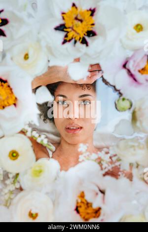 Giovane donna sdraiata sotto una superficie di vetro con fiori Foto Stock