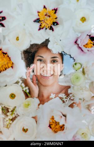 Donna sorridente giacente sotto una superficie di vetro con fiori Foto Stock