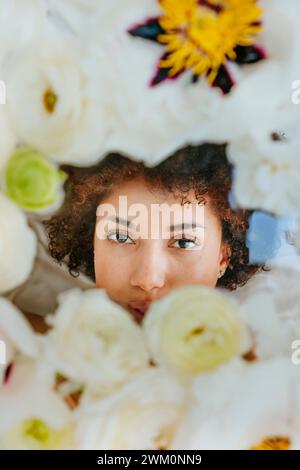 Giovane donna dietro una superficie di vetro con fiori Foto Stock