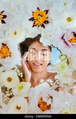 Giovane donna con gli occhi chiusi giacente sotto una superficie di vetro con fiori Foto Stock