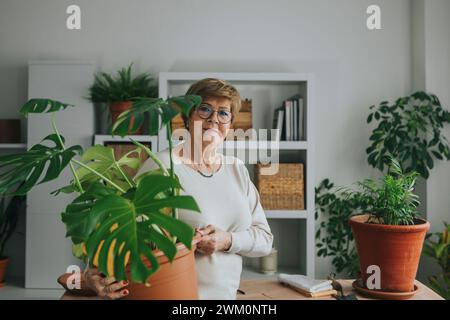 Donna sorridente che tiene in mano la pianta di monstera a casa Foto Stock