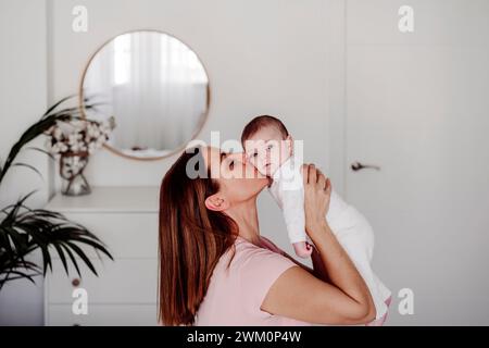 Donna che tiene e bacia figlia a casa Foto Stock