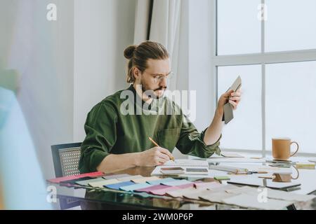 Designer di mobili che tiene campioni di colore e lavora alla scrivania in ufficio Foto Stock
