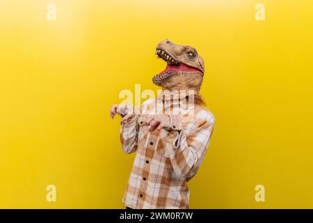 Uomo con maschera di dinosauro e gesti davanti al muro giallo Foto Stock