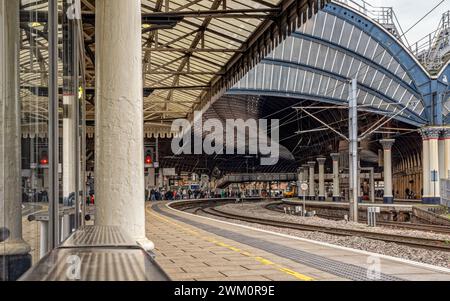 Uno storico arco metallico copre l'ingresso di una stazione ferroviaria. Un treno e i passeggeri stanno ai binari e una colonna è in primo piano. Foto Stock