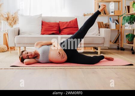 Donna incinta sdraiata sul tappetino yoga che si esercita a casa Foto Stock