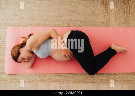Donna incinta sdraiata sul tappetino per esercizi a casa Foto Stock