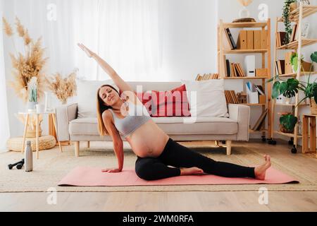 Donna incinta che si allunga la mano praticando yoga sul tappetino per esercizi Foto Stock