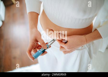 Donna che inietta una penna per insulina nello stomaco a casa Foto Stock