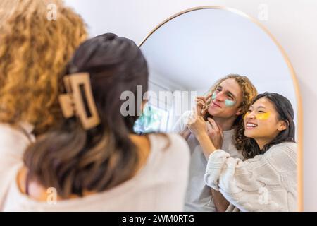 Coppia felice che applica patch per la cura della pelle sotto gli occhi davanti allo specchio a casa Foto Stock