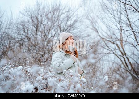 Donna felice che indossa un cappello in maglia tra gli alberi in inverno Foto Stock
