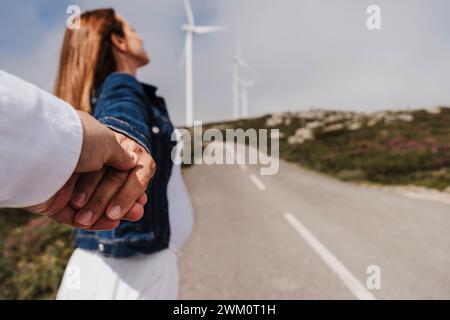 Spagna, Madrid, coppia che si tiene per mano lungo la strada che si estende oltre il parco eolico Foto Stock