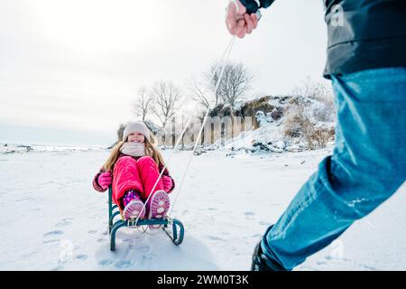 Padre che cavalca figlia seduta sulla slitta in inverno Foto Stock