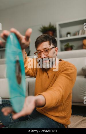 Uomo che mostra un disco vecchio stile seduto in salotto Foto Stock