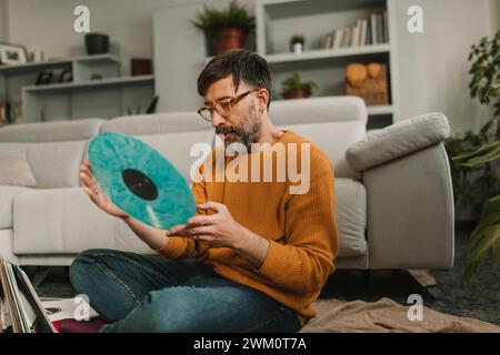 Uomo che guarda un disco vecchio stile seduto in salotto Foto Stock