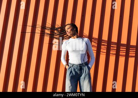 Giovane donna sorridente che lancia i capelli davanti al muro Foto Stock