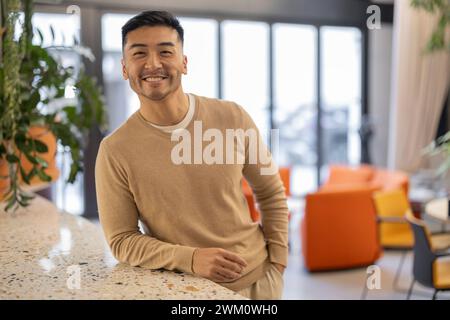 Sorridente giovane uomo d'affari che si appoggia all'ufficio Foto Stock