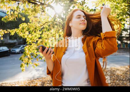 Bella donna rossa che ascolta musica in autunno Foto Stock