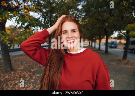 Donna sorridente che indossa un maglione rosso in autunno Foto Stock