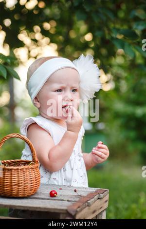 Con un'attenta supervisione, l'adorabile bambino esplora i sapori della natura, assaggiando per la prima volta le ciliegie tra i fiori profumati del c Foto Stock