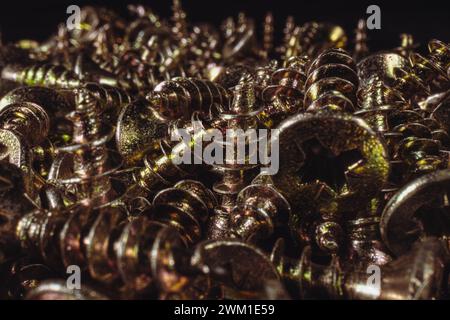 Un mucchio di viti metalliche gialle su sfondo nero. Sfondo delle viti metalliche. Foto Stock
