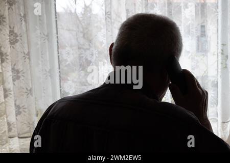 Telefonbetrug oder Einsamkeit bei älteren Menschen Ein älterer Mann steht vor einem Fenster mit dem Telefon am Ohr und schaut hinaus. Symbolbild Moritzburg Sachsen Deutschland *** frode telefonica o solitudine tra gli anziani un uomo anziano si trova di fronte a una finestra con il telefono rivolto all'orecchio e guarda all'immagine simbolica Moritzburg Sassonia Germania Daniel Schäfer Foto Stock