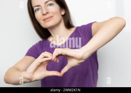 Ispira l'inclusione. Donna che tiene le mani a forma di cuore e le tiene davanti a sé, t-shirt viola vestita. Giornata internazionale delle donne Foto Stock