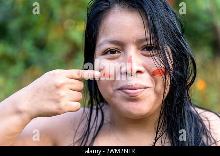 Bella donna della tribù di Embera che mette dipinti rossi tradizionali sul suo viso, il parco nazionale di Chagres, Panama Foto Stock
