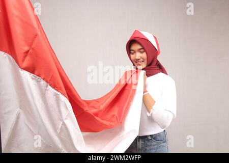 Ritratto di una donna che indossa un hijab asiatico con una camicia bianca che bacia la bandiera rossa e bianca indonesiana su uno sfondo bianco. Concetto di Indonesia Foto Stock