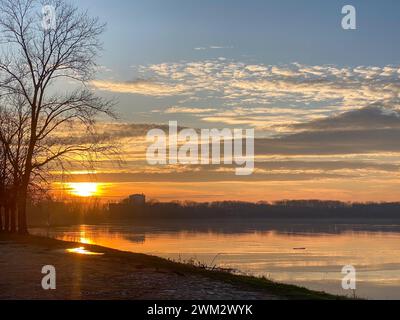 Fiume po e vibrante tramonto sullo sfondo. Il cielo è dipinto in sfumature di arancione, che riflettono l'acqua increspata. San Nazzaro, PC, Italia Foto Stock