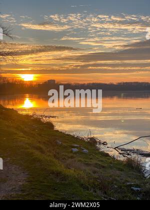 Fiume po e vibrante tramonto sullo sfondo. Il cielo è dipinto in sfumature di arancione, che riflettono l'acqua increspata. San Nazzaro, PC, Italia Foto Stock